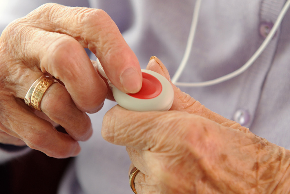 An older lady is holding a LifeLine pendant in both hands, with one finger on the red button 