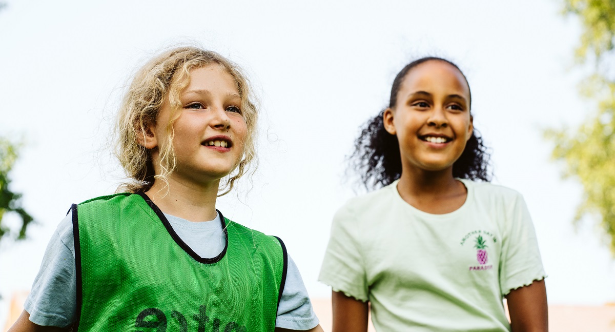 Two 10 year old girls smile as they take part in a sports game outside